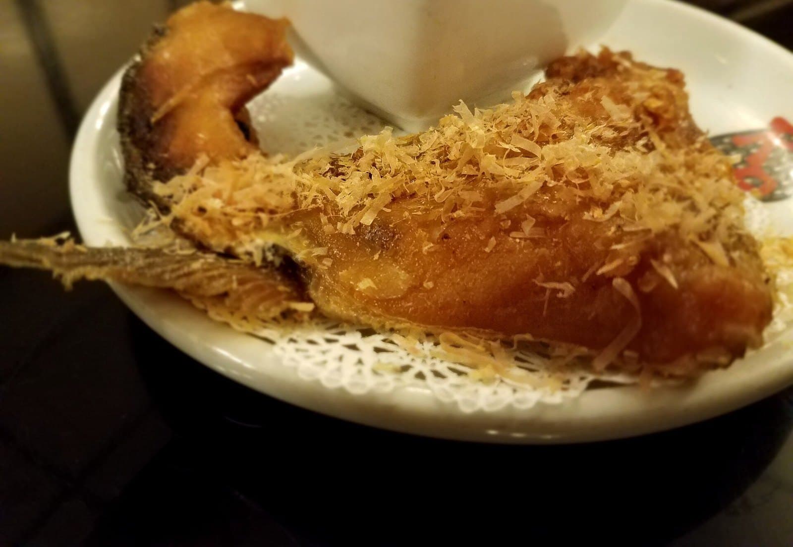 A grilled fish collar on a white plate, topped with bonito flakes